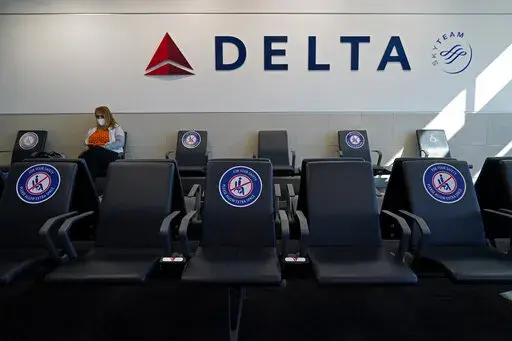 A passenger wears a face mask as she waits in a socially-distance area for a Delta Airlines flight, Wednesday, Feb. 3, 2021, at Hartsfield-Jackson International Airport in Atlanta.  Delta Air Lines will start paying flight attendants during the time that passengers are boarding. That's a first for a major U.S. airline. Flight attendants in the U.S. generally don't begin getting paid until the doors close after boarding. Delta said Tuesday, April 26, 2022, that the change will take effect in June