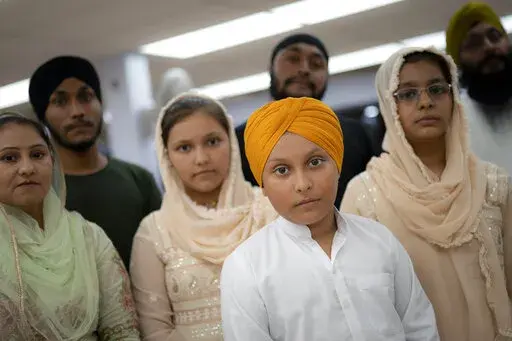 Amandeep Singh, 12, stands with his family in the communal room where "langar," food served after temple services, is provided at Guru Nanak Darbar of Long Island, a Sikh gurdwara, Wednesday, Aug. 24, 2022, in Hicksville, N.Y. Their Afghan Sikh family of 13 has found refuge in the diaspora community on Long Island where the Sikh community is helping family members obtain work permits, housing, healthcare and find schools for the children. (AP Photo/John Minchillo)