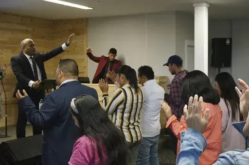 The Rev. Gustavo Castillo leads in song and praise members of his congregation at the Iglesia Pentecostal Unida Latinoamericana in Columbia Heights, Minn., on Sunday, Sept. 24, 2023. Even though a sudden change in how the U.S. government processes some green cards is threatening the Colombia-born pastor's ability to stay in the country, his dedication to his mostly migrant flock is undaunted, Castillo said. (AP Photo/Giovanna Dell'Orto)