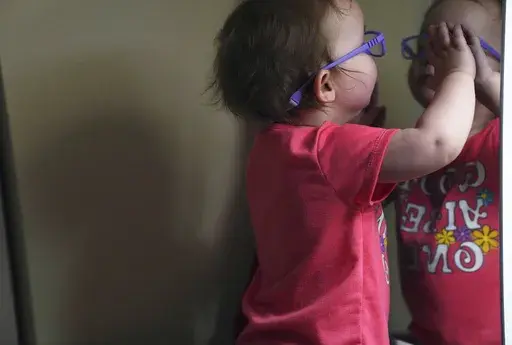 The Hackneys’ daughter looks at her reflection in a bedroom mirror during a supervised visit at her parent's home in Oakdale, Pa., on Thursday, Nov. 17, 2022. At 8 months old, the young child was taken from her parents custody after arriving at the hospital severely dehydrated and malnourished. The Hackneys and their lawyer believe the Allegheny County Family Screening tool may have flagged the couple as dangerous because of their disabilities. (AP Photo/Jessie Wardarski)