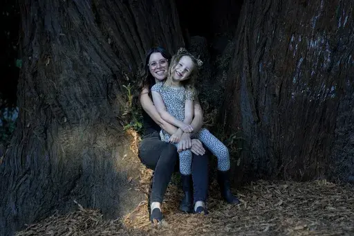 Hannah Levy holds her daughter, Aylah, 6, at Codornices Park, a location Aylah attended as a Berkeley Forest School student, during an interview in Berkeley, Calif., Wednesday, Nov. 8, 2023. Some parents like Levy don't see much value in traditional kindergarten. She wanted Aylah to enjoy being a kid. There is plenty of time, she reasoned, for her daughter to develop study skills. (AP Photo/Jeff Chiu)