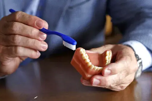 A dentist holds a model of teeth and a toothbrush in Seattle on Friday, Aug. 3, 2018. For many years, studies have shown that gum diseases are tied to premature birth. Scientists believe bacterial infections in the mouth can increase inflammation in the body, which could lead to early birth. (AP Photo/Elaine Thompson, File)