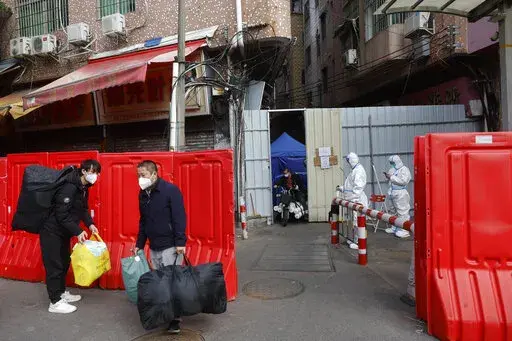Migrant workers with their belongings leave a barricaded village after authorities' easing of COVID-19 curbs in Haizhu district in Guangzhou in south China's Guangdong province on Friday, Dec. 2, 2022. Local Chinese authorities on Saturday announced a further easing of COVID-19 curbs, with major cities such as Shenzhen and Beijing no longer requiring negative tests to take public transport. (Chinatopix Via AP)