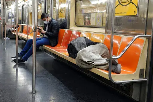 A man sleeps on subway train seats, in New York, on April 14, 2021.New York Mayor Eric Adams is announcing a plan to boost safety in the city's sprawling subway network and try to stop homeless people from sleeping on trains or living in stations. (AP Photo/Richard Drew, File)
